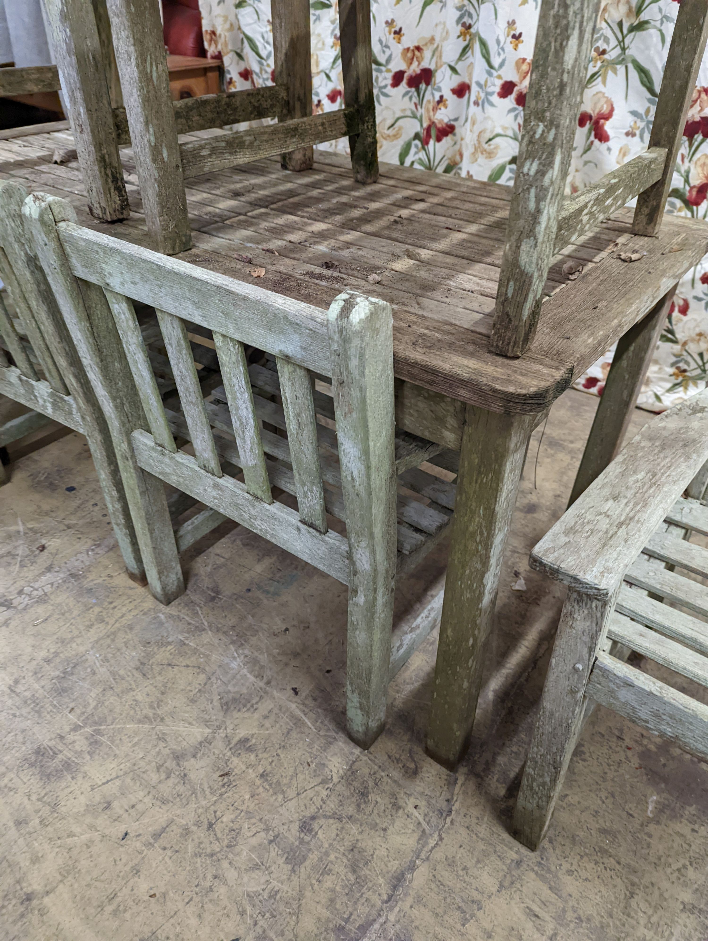 A weathered teak rectangular garden table and six elbow garden chairs, not matching. Table measures, W-149cm, D-70cm, H-75cm.